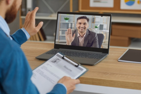 Entrevista de trabajo virtual, el entrevistador tiene un CV en la mano el entrevistado aparece en un portátil