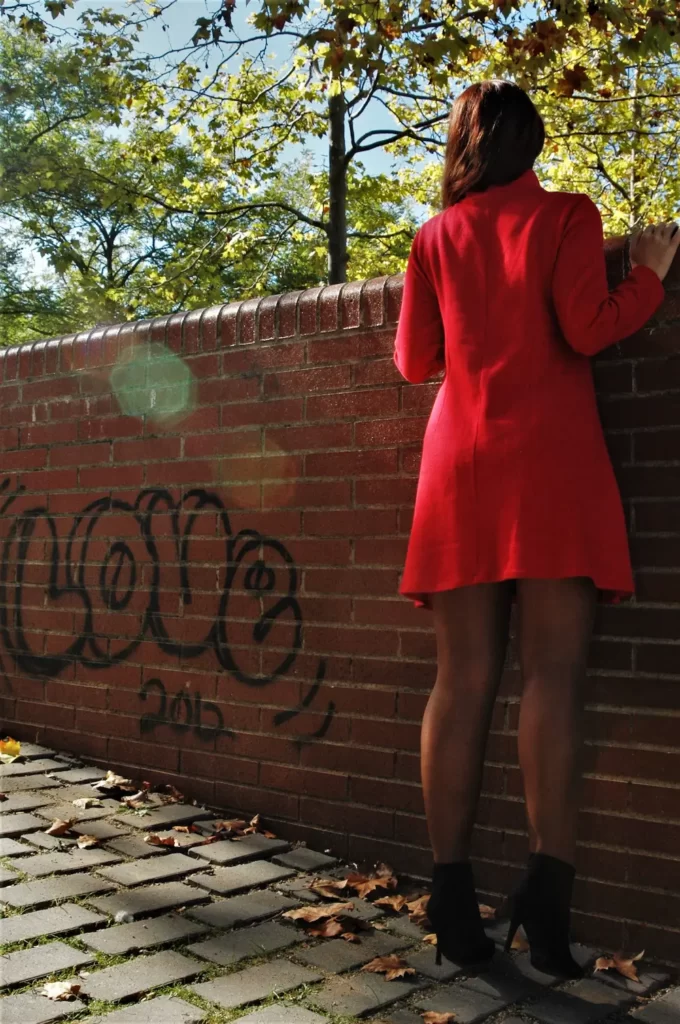 Mujer con un vestido rojo de la Nina de Paper mirando por un muro.  Pide el vestido con el presupuesto ropa mujer.
