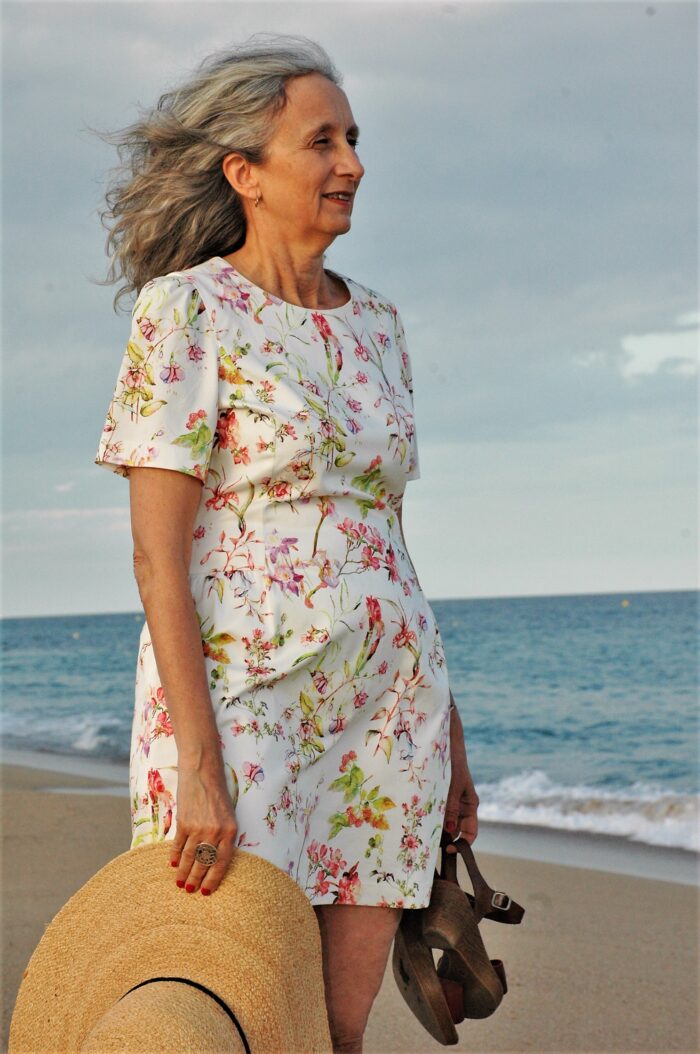 vestido estampado de verano, aparece una mujer en la playa con el vestido un sombrero y unos zapatos en la mano